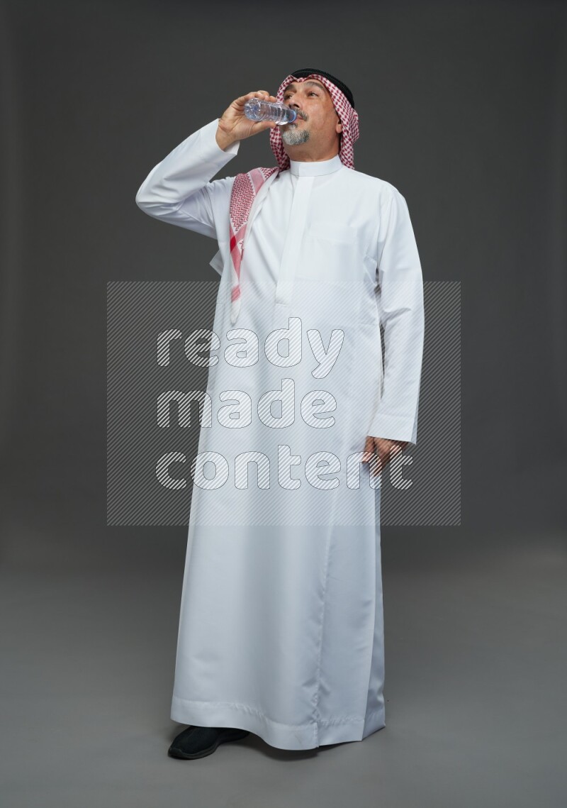 Saudi man with shomag Standing drinking water on gray background