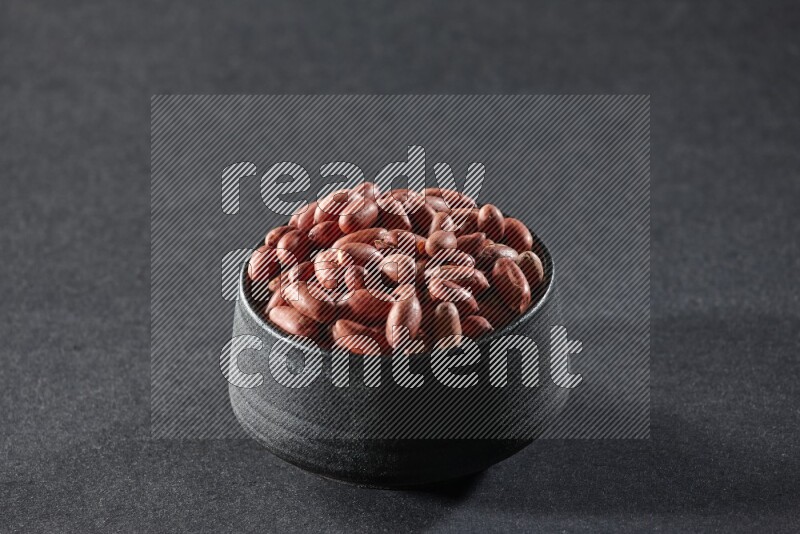 A black pottery bowl full of red skin peanuts on a black background in different angles