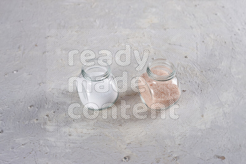 2 glass jars one is full of fine himalayan salt and the other with table salt on white background