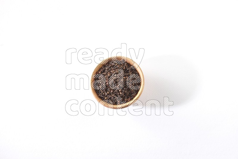 A wooden bowl full of cloves on a white flooring