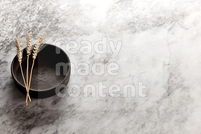 Wheat stalks on Black Pottery Oven Plate on grey marble flooring, 45 degree angel