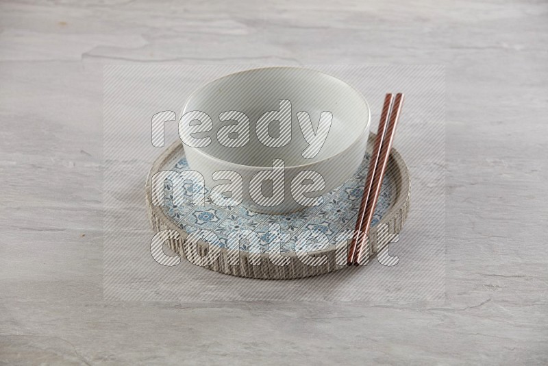 white pottery round bowl on top of multi color round ceramic plate and chopsticks, on grey textured countertop