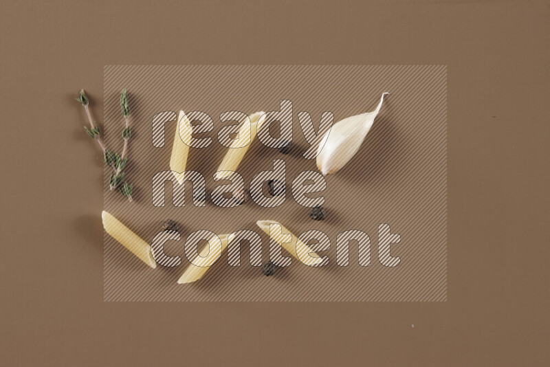 Raw pasta with different ingredients such as cherry tomatoes, garlic, onions, red chilis, black pepper, white pepper, bay laurel leaves, rosemary and cardamom on beige background