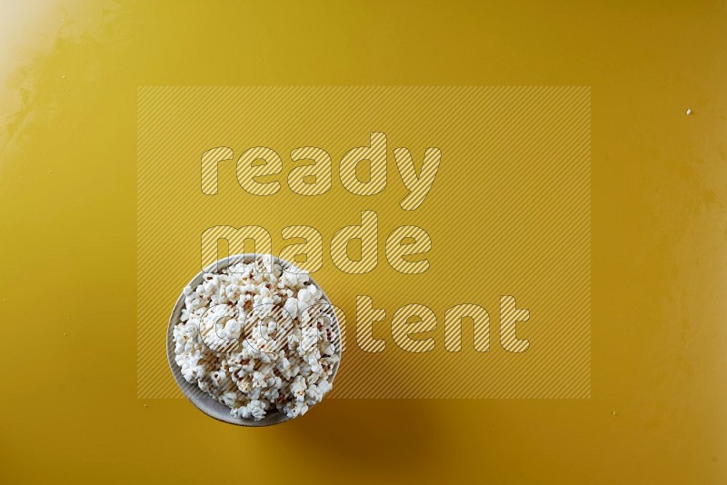 A white pottery bowl full of popcorn on a yellow background in different angles