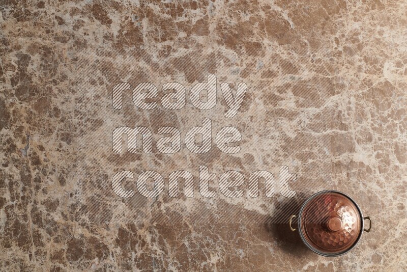 A small copper pot on beige marble background