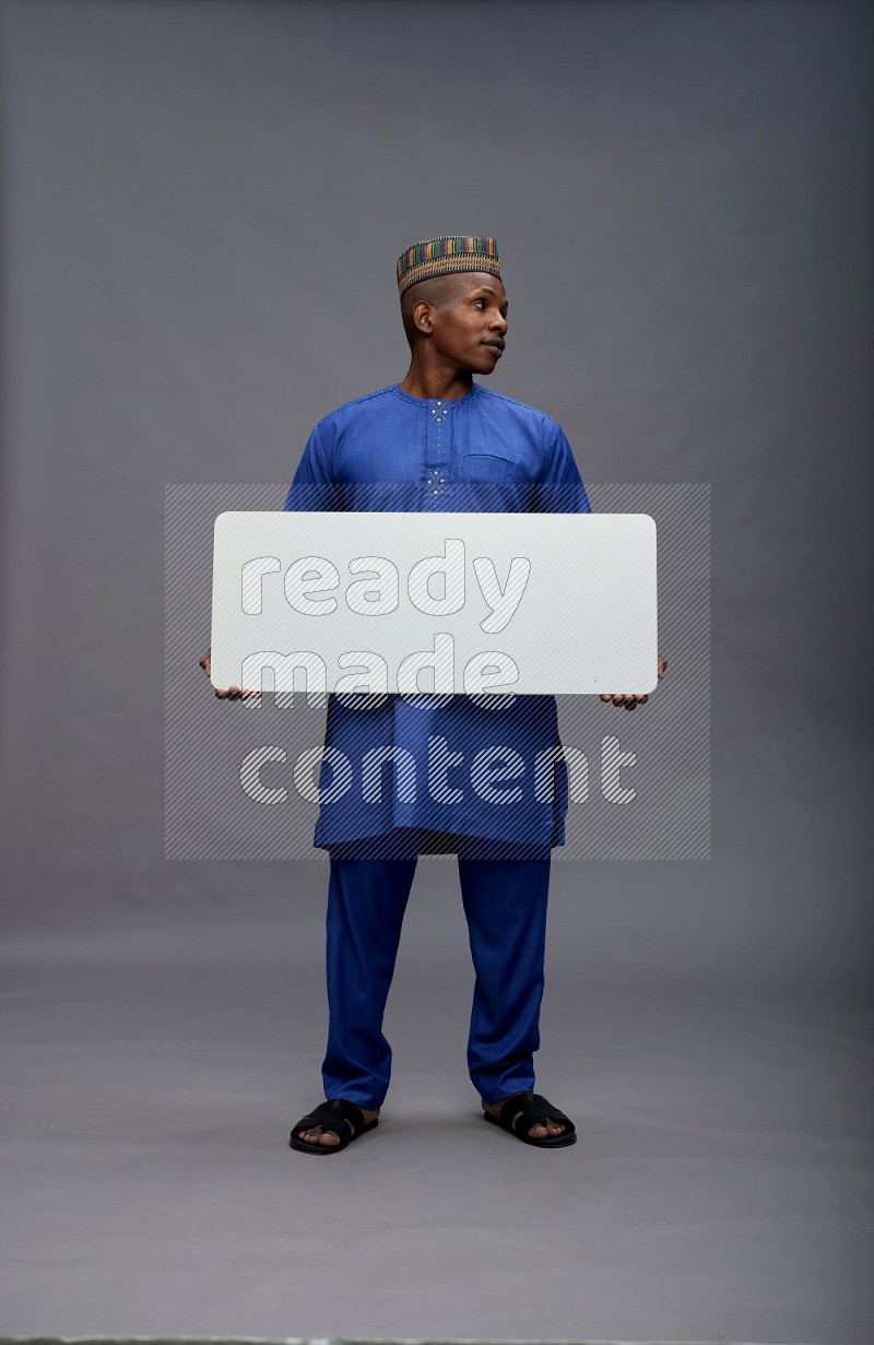 Man wearing Nigerian outfit standing holding board on gray background