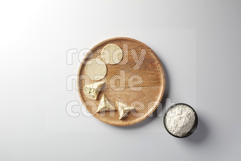 two closed sambosas and one open sambosa filled with cheese while flour aside in a wooden dish on a white background