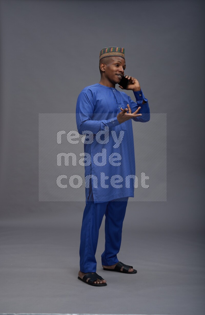 Man wearing Nigerian outfit standing talking on phone on gray background