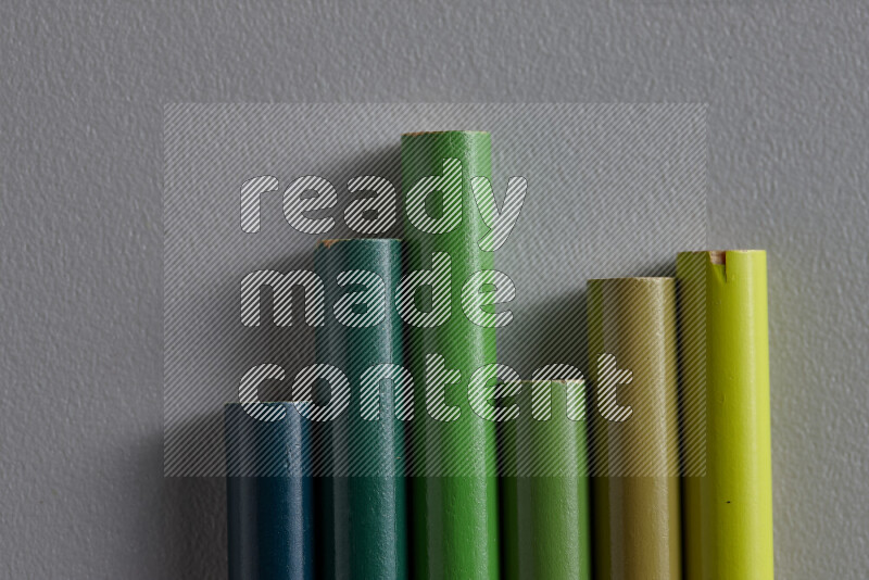 A collection of colored pencils arranged showcasing a gradient of green hues on grey background