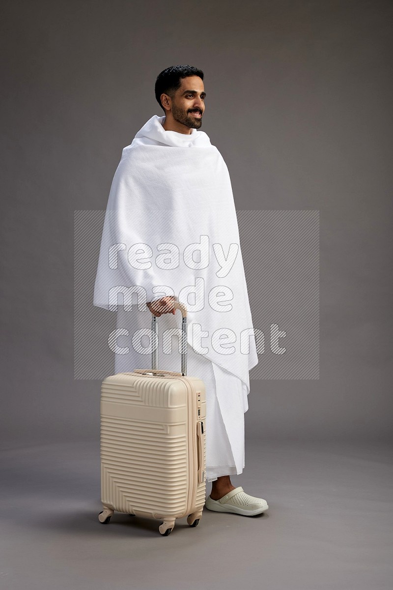 A man wearing Ehram Standing holding traveling bag on gray background