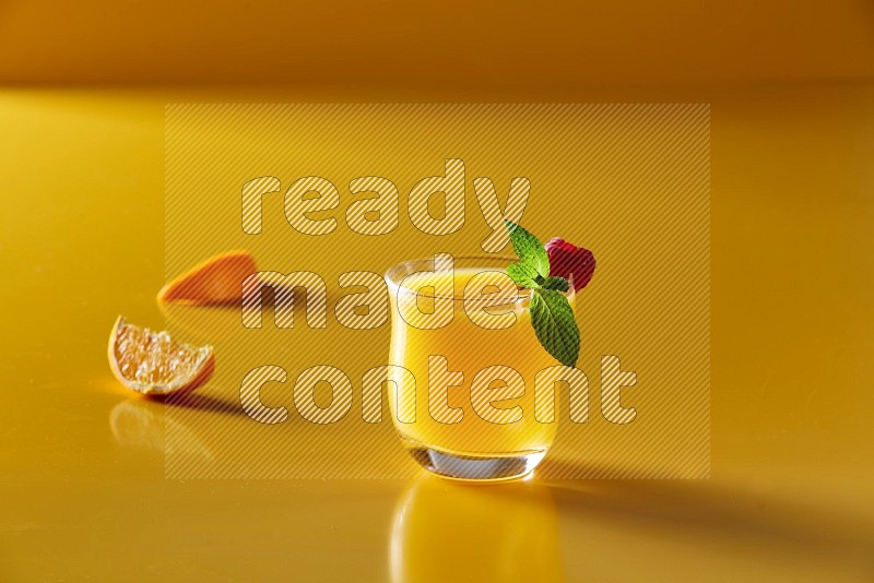 glass of orange juice with berry & mint on yellow background