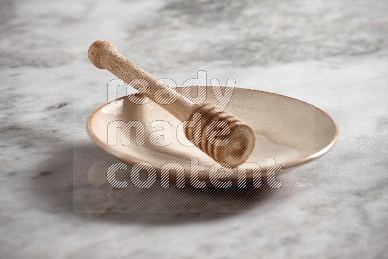 Beige Pottery Plate with wooden honey handle in it, on grey marble flooring, 15 degree angle