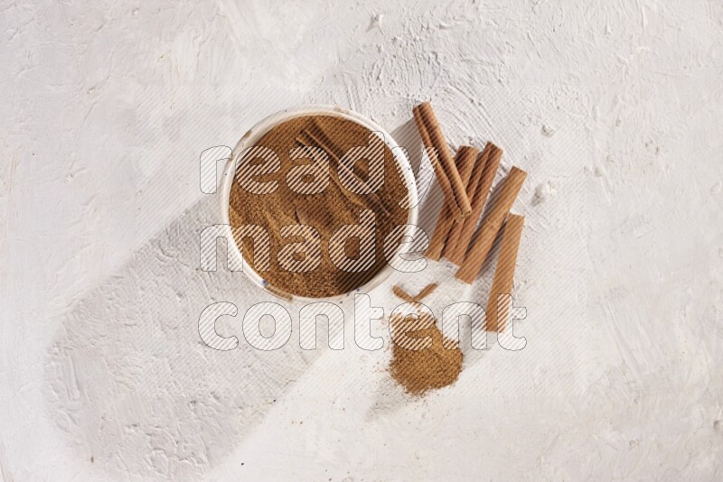 Ceramic bowl full of cinnamon powder with cinnamon sticks on the side on white background