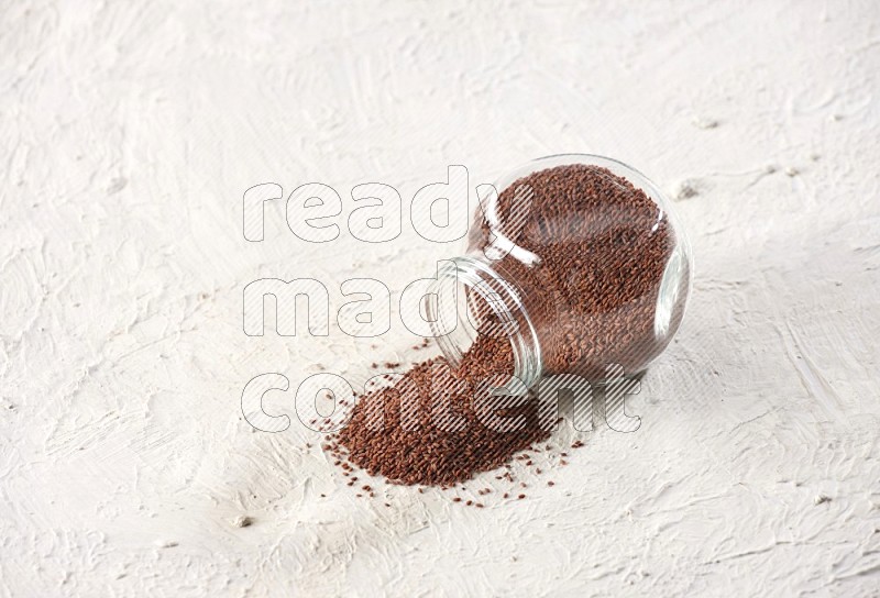 A glass spice jar full of garden cress seeds and jar is flipped with fallen seeds on a textured white flooring