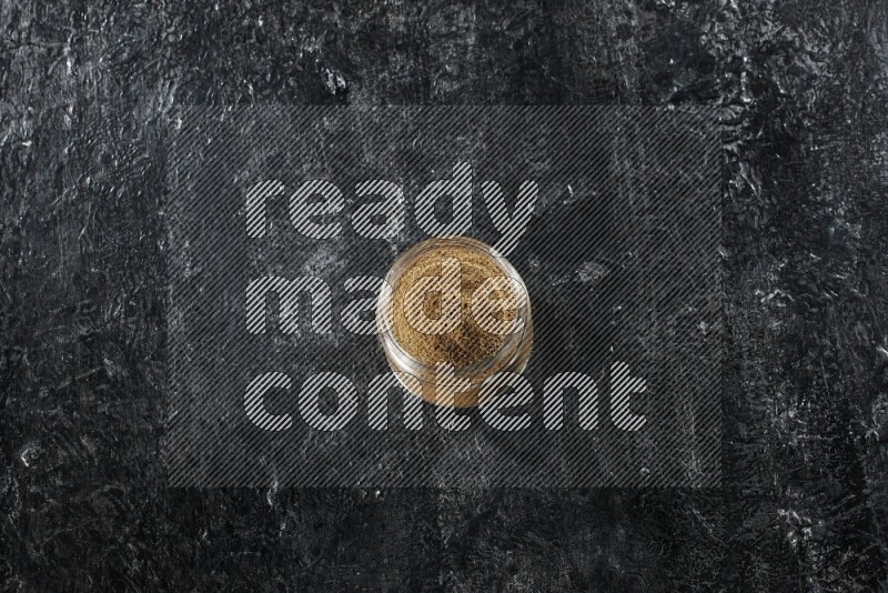 وعاء زجاجي ممتلئ ببودرة الكمون على خلفية سوداء