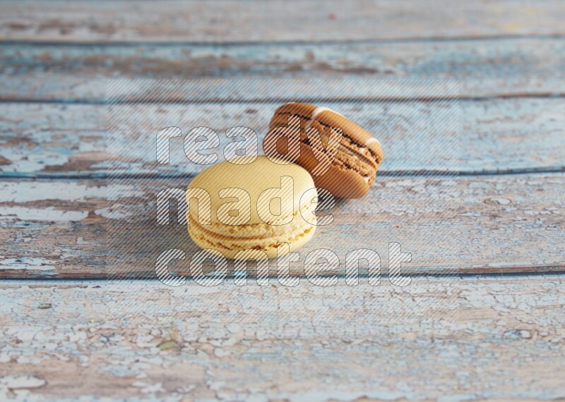 45º Shot of of two assorted Brown Irish Cream, and Yellow Vanilla macarons on light blue background