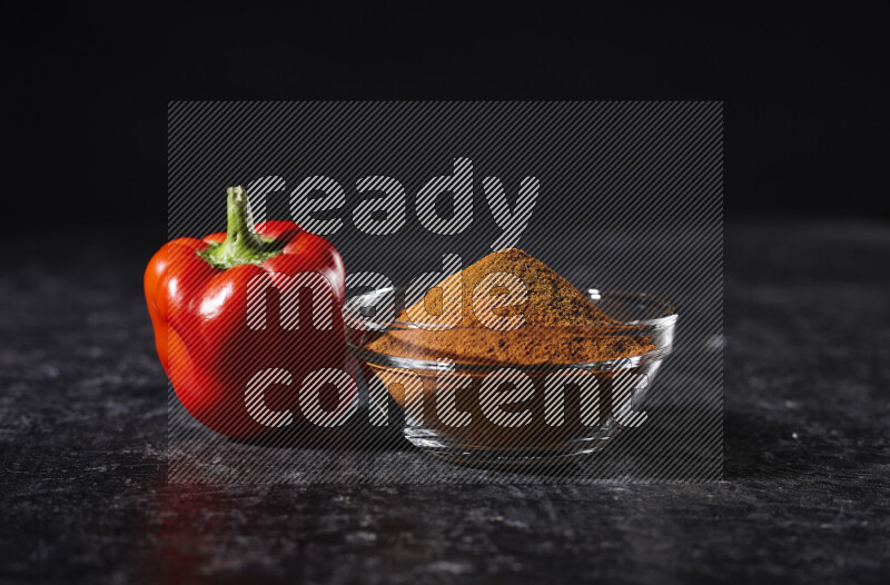 A glass bowl full of ground paprika powder on black background