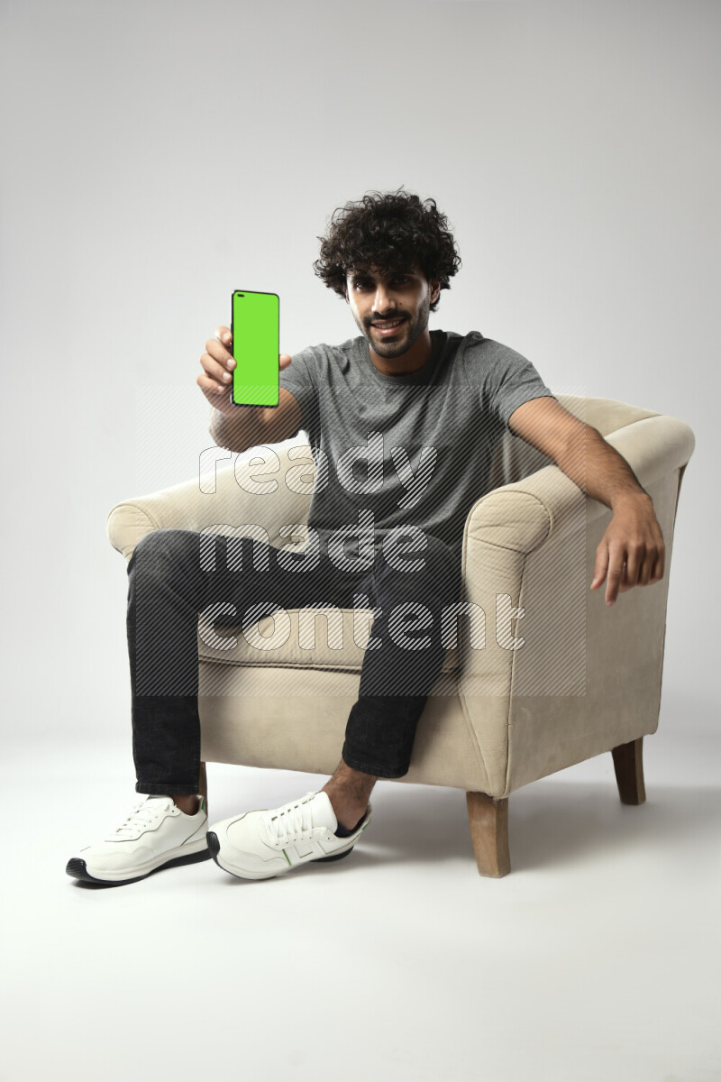 A man wearing casual sitting on a chair showing a phone screen on white background