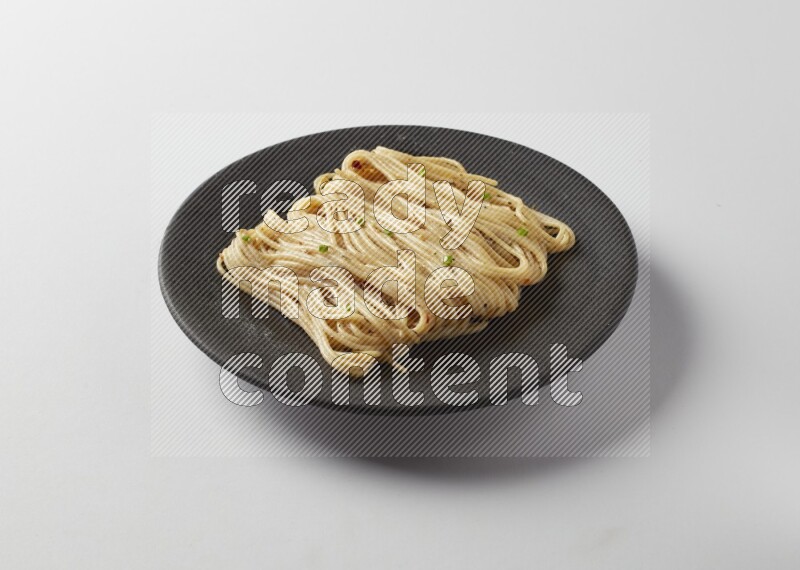 spaghetti pasta with white sauce on a black plate on a white background