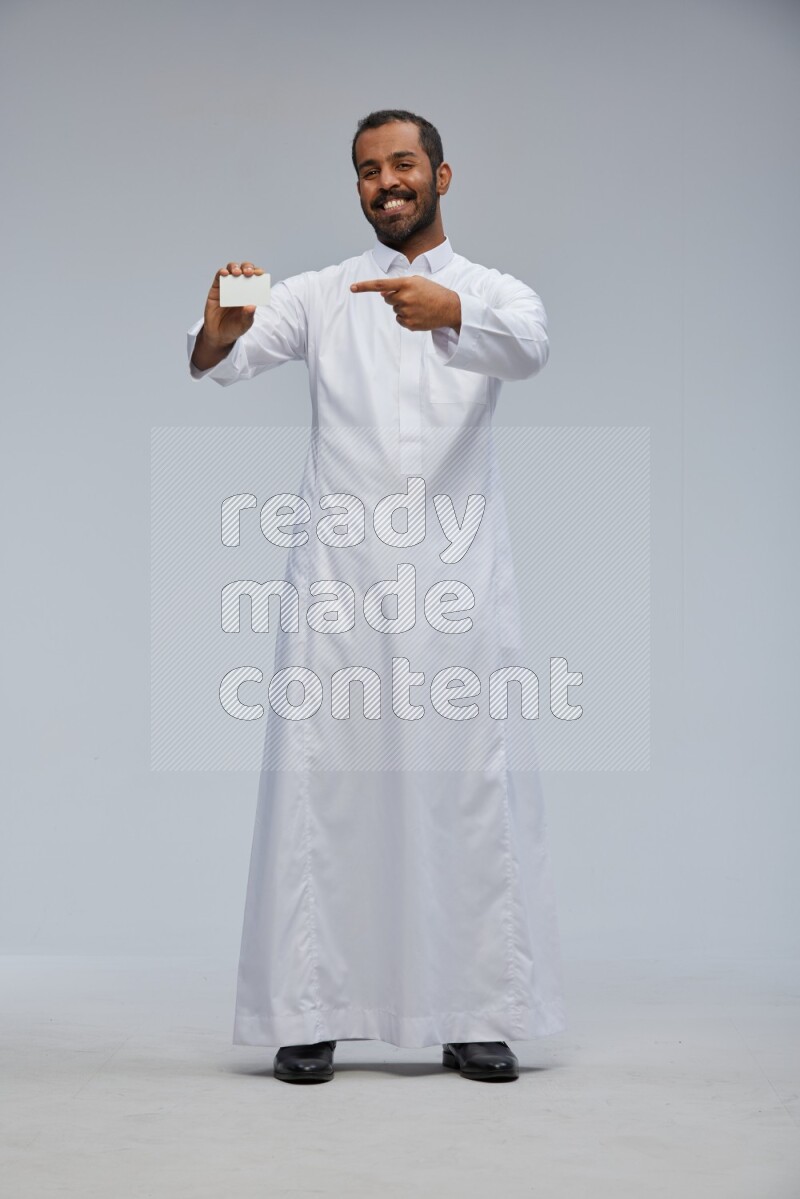 Saudi man wearing Thob standing holding ATM card on Gray background