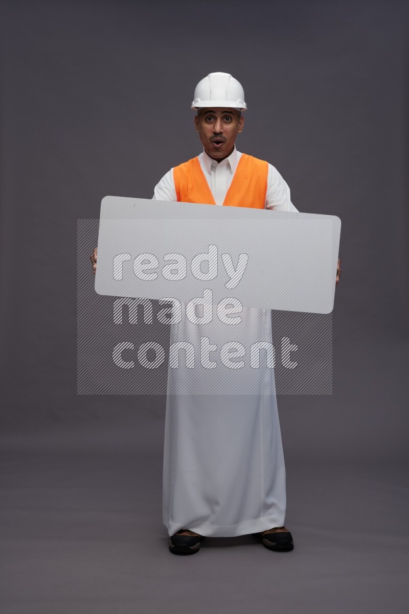 Saudi man wearing thob with engineer vest standing holding board on gray background