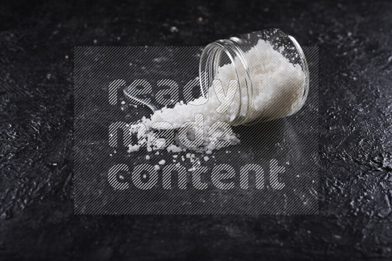 A glass jar full of coarse sea salt crystals on black background