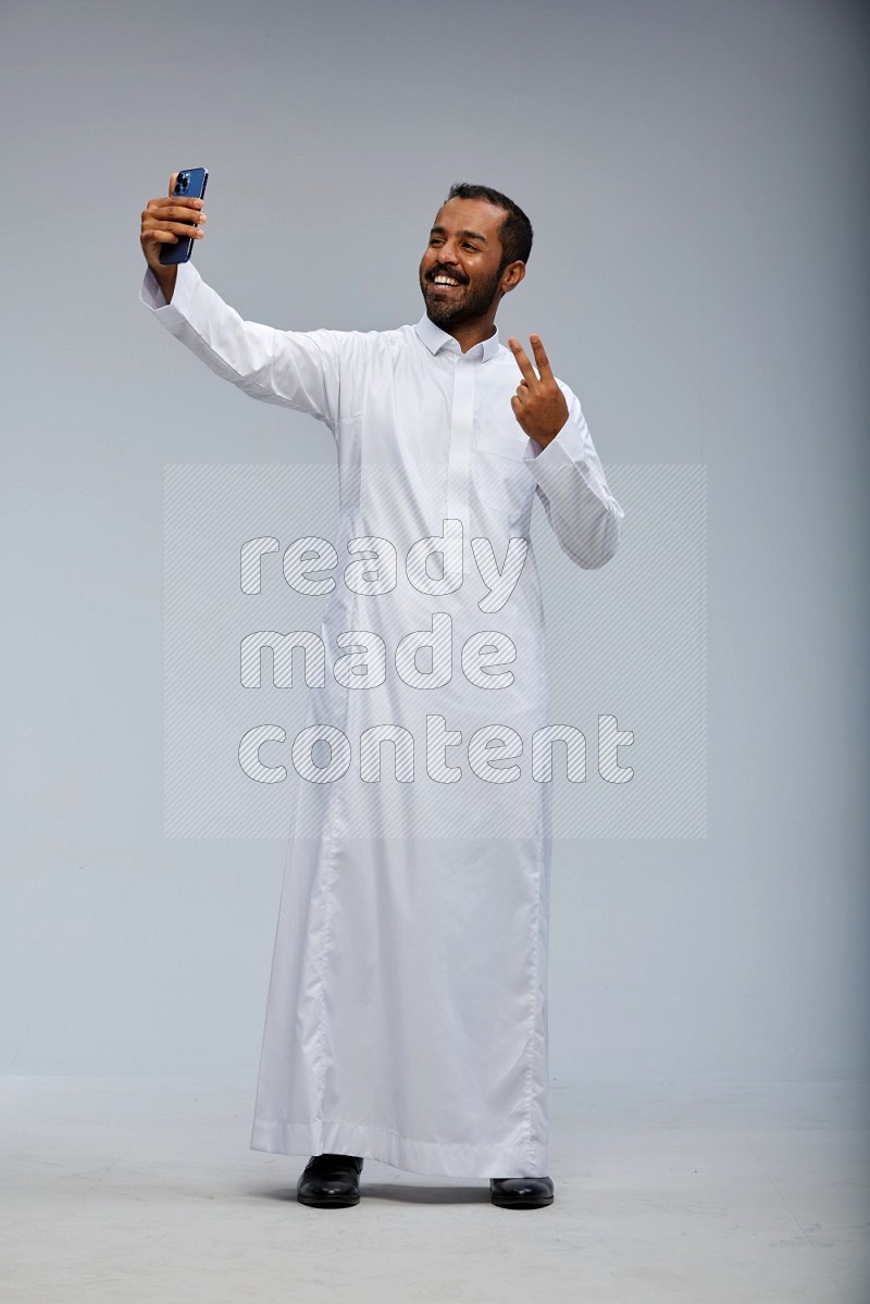 Saudi man wearing Thob standing taking selfie on Gray background