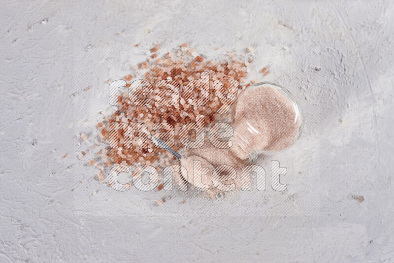 A glass jar full of fine himalayan salt with some himalayan crystals beside it on a white background