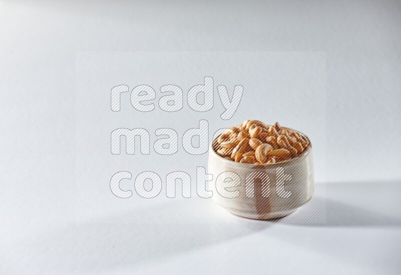 A beige ceramic bowl full of cashews on a white background in different angles
