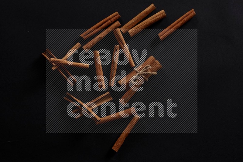 4 Cinnamon sticks stacked and bounded with more sticks in the background on black flooring