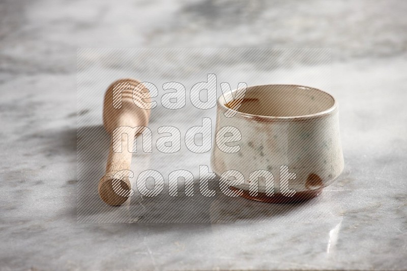 Multicolored Pottery bowl with wooden honey handle on the side with grey marble flooring, 15 degree angle