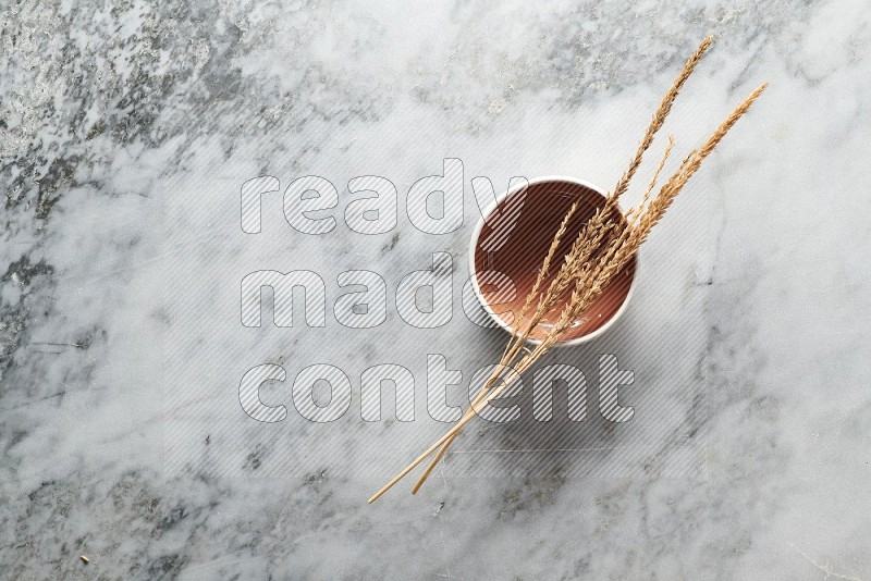 Wheat stalks on Brown Pottery Bowl on grey marble flooring, Top view