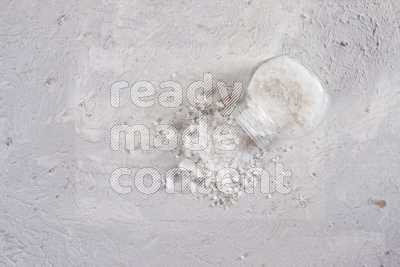 A glass jar full of coarse sea salt crystals on white background