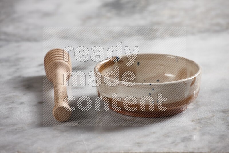 Multicolored pottery bowl with wooden honey dipper on the side on grey marble background