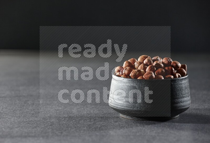A black pottery bowl full of peeled hazelnuts on a black background in different angles