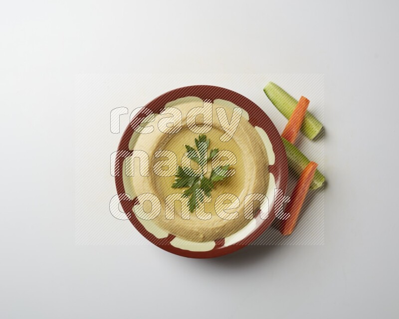 Hummus in a traditional plate garnished with parsley on a white background