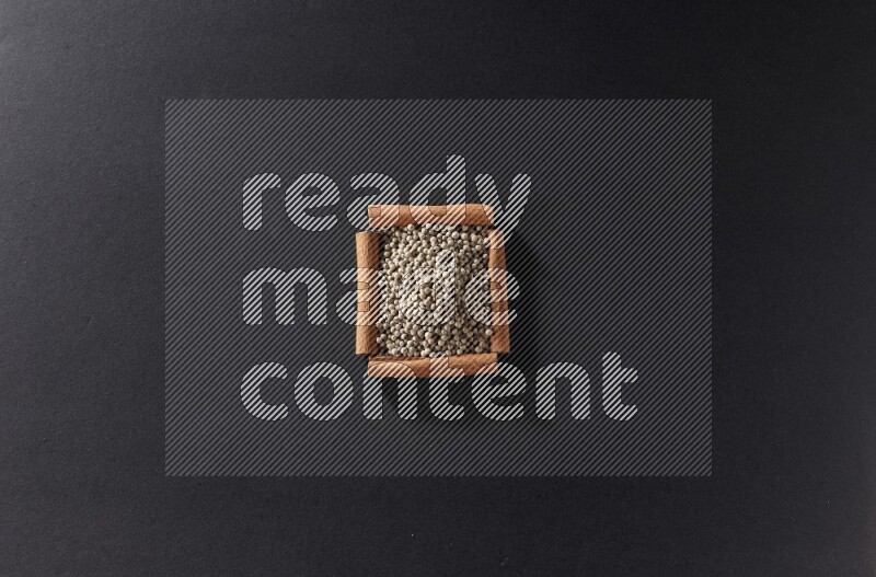 A single square of cinnamon sticks full of white pepper on black flooring