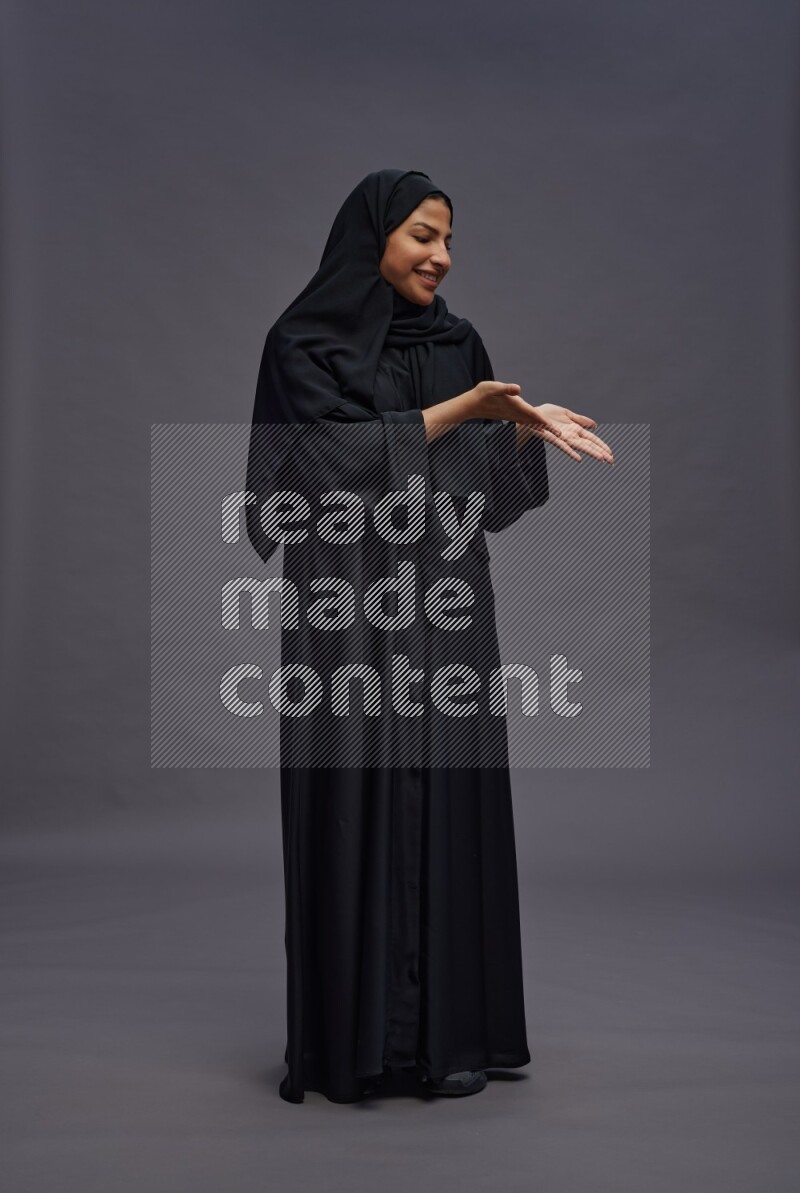 Saudi woman wearing Abaya standing interacting with the camera on gray background