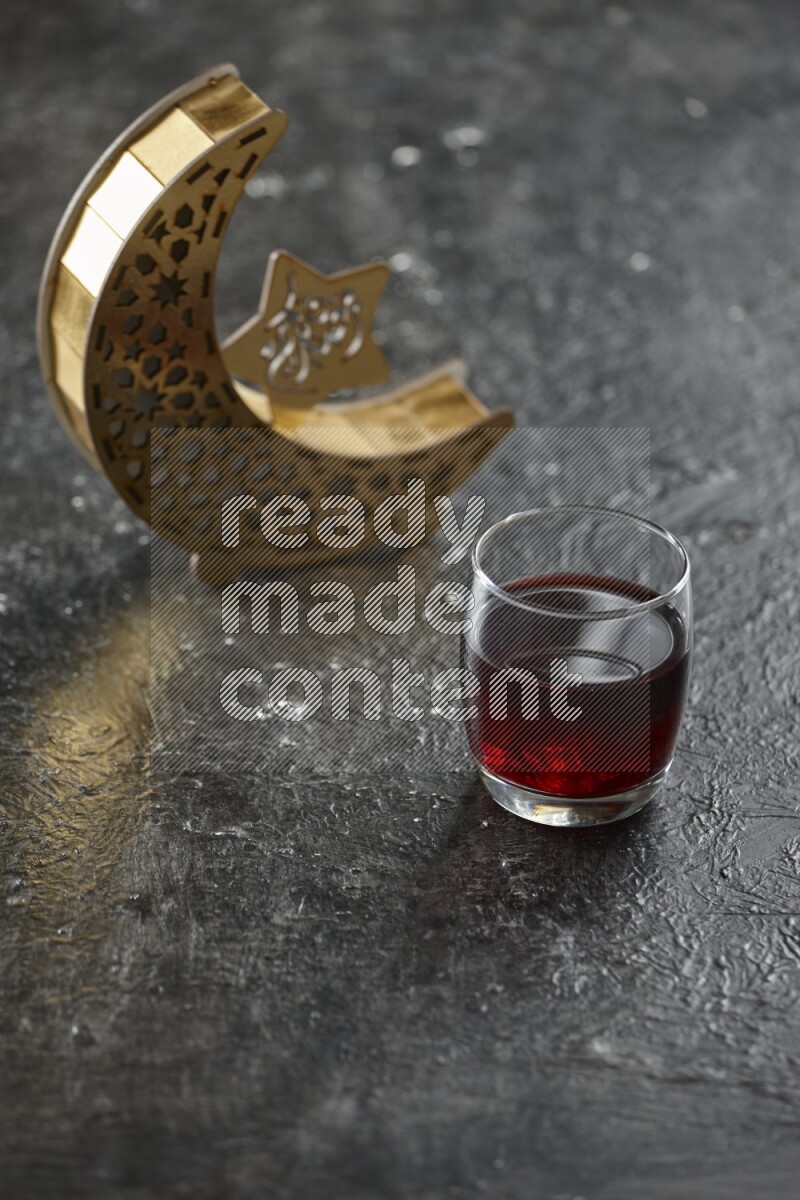 A wooden golden crescent lantern with different drinks, dates, nuts, prayer beads and quran on textured black background