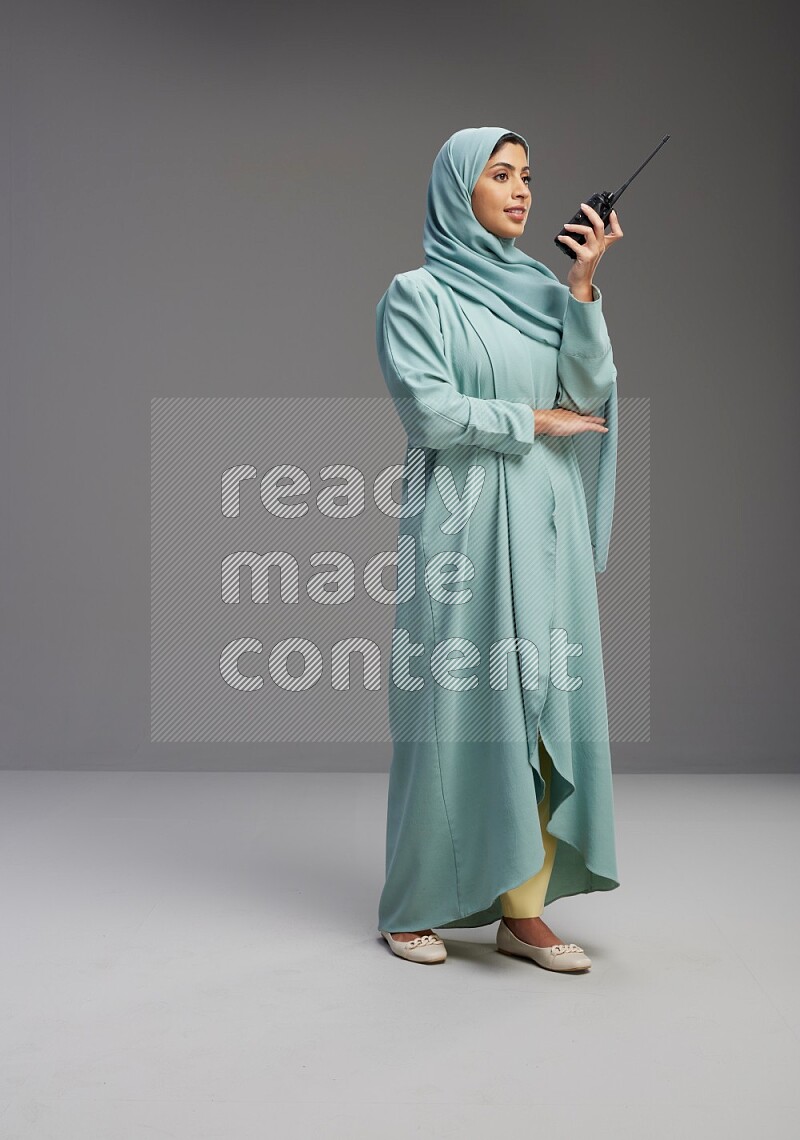 Saudi Woman wearing Abaya standing holding walkie-talkie on Gray background