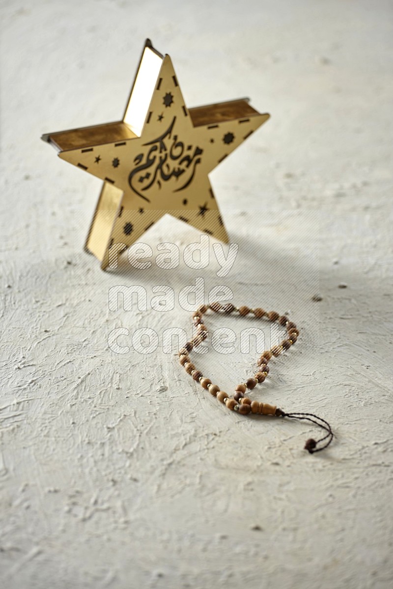 A wooden golden star lantern with different drinks, dates, nuts, prayer beads and quran on textured white background