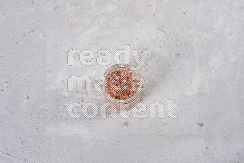 A glass jar full of coarse himalayan salt crystals on white background