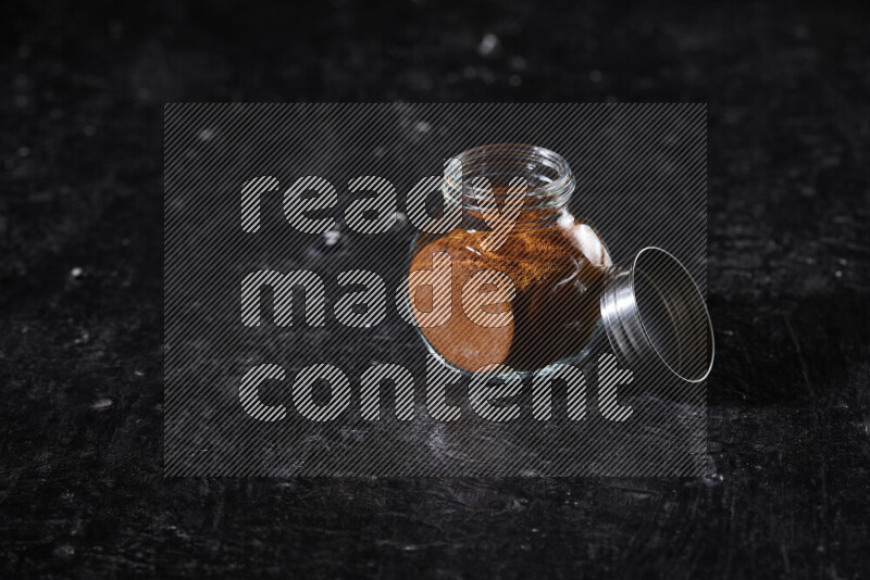 A glass jar full of ground paprika powder on black background