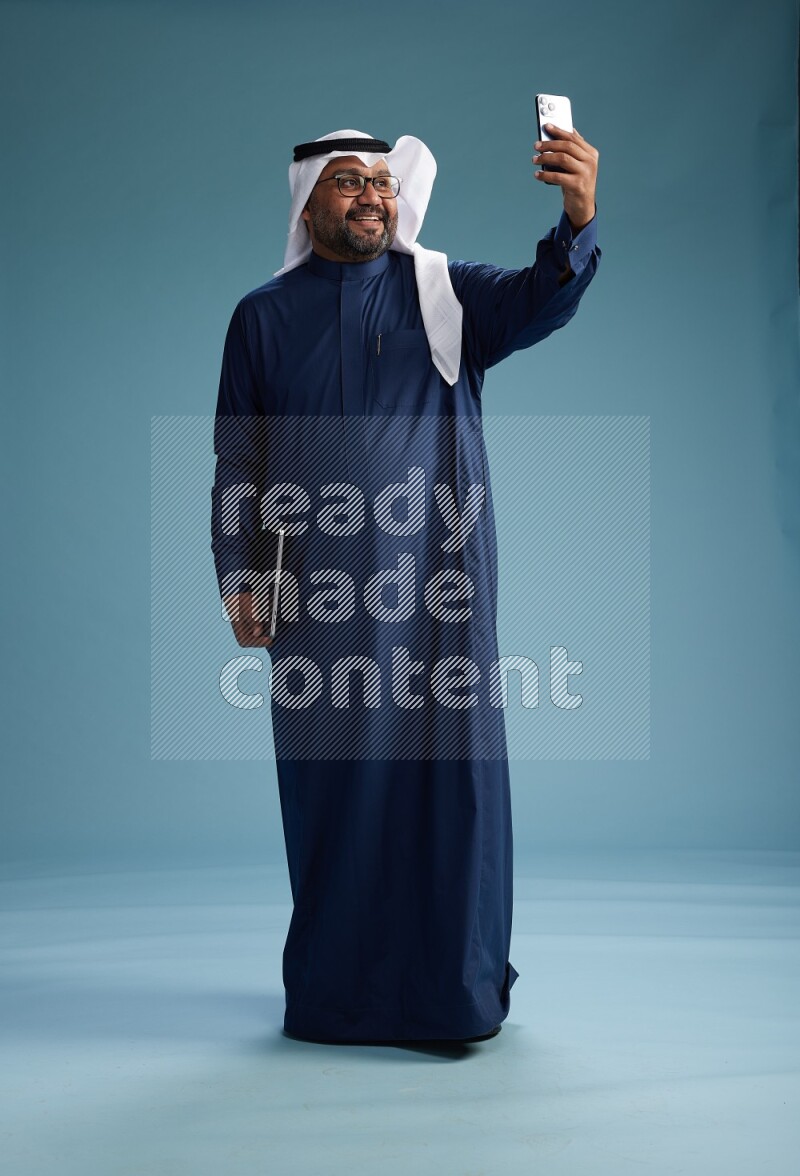 Saudi Man with shimag Standing taking selfie on blue background