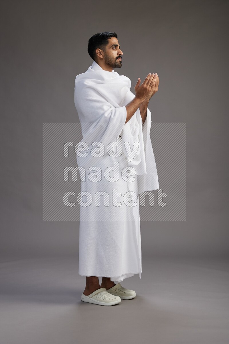A man wearing Ehram Standing performing dua'a on gray background