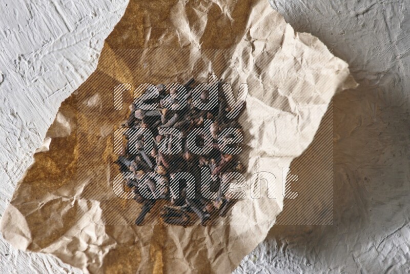 Cloves on crumpled piece of paper on a textured white flooring