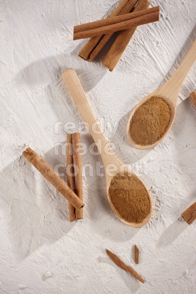 Two wooden spoons full of cinnamon powder with cinnamon sticks on white background