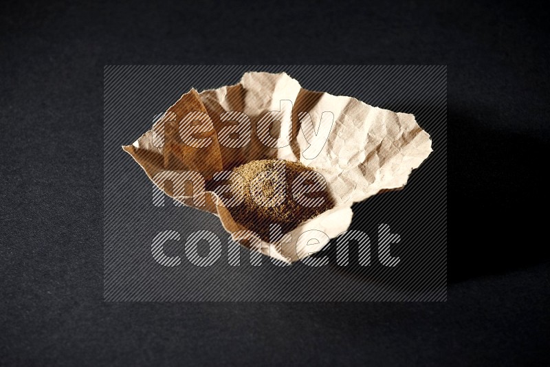 Cumin powder in a crumpled piece of paper on black flooring