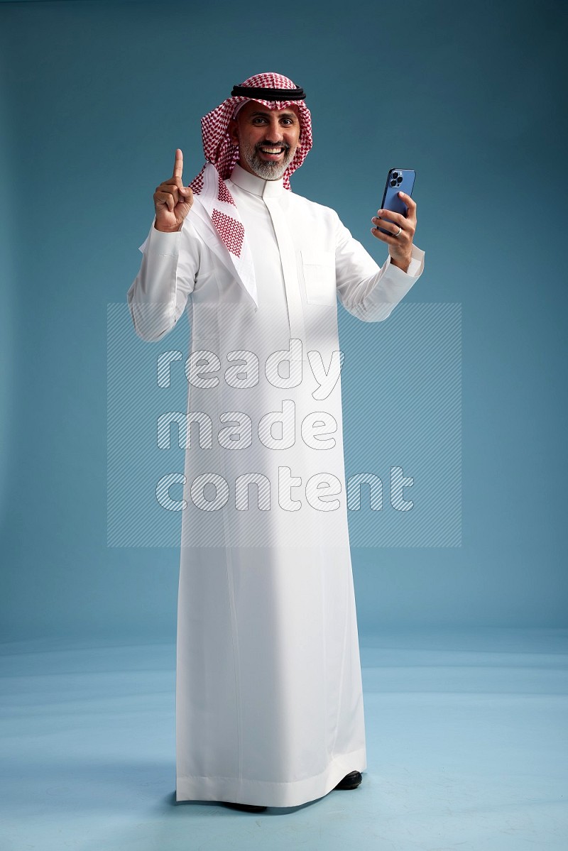 Saudi man wearing thob and shomagh texting on blue background