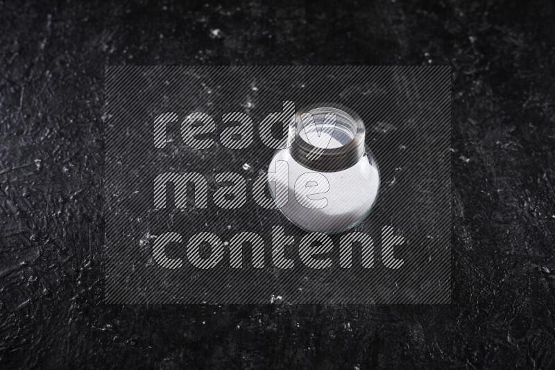 A glass jar full of fine table salt on black background